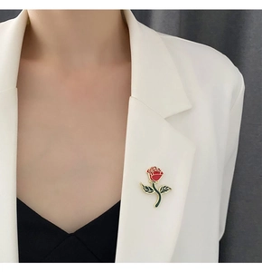 Detailed shot of a red rose brooch with golden stem on a white blazer lapel