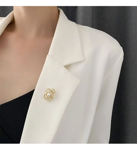 Gros plan d'une broche camélia dorée avec perles sur le revers d'un tailleur blanc