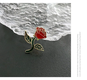 Detail of red rose enamel brooch with gold metallic edges on a textured glass plate