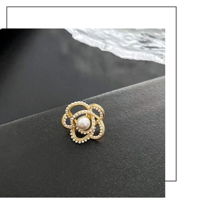 Gros plan sur la broche camélia avec perles blanches sur base dorée et texture noire
