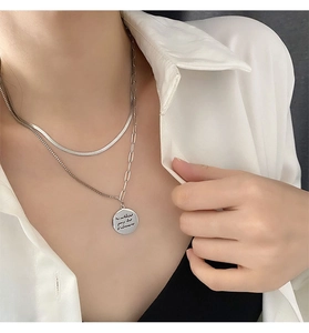 Close-up of double-layer silver necklace with lettered round pendant on a white shirt