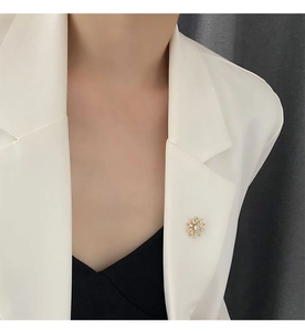 Détail d'une élégante broche fleur dorée avec perles et cristal sur blazer blanc