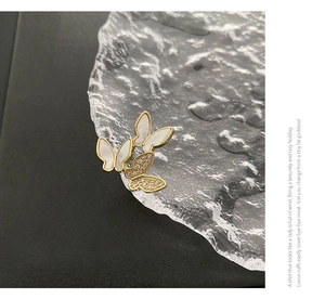 Detail of three-butterfly brooch featuring white shell wings and inlaid crystals on gold finish
