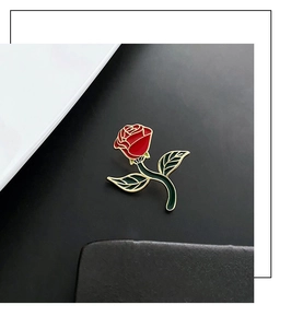 Macro detail of a red rose brooch with green leaves and gold-plated metallic edges