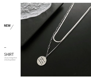 Macro detail of layered silver snake chain necklace and engraved round coin pendant
