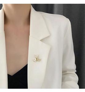 Detailed close-up of three butterfly shell brooches worn on a white suit lapel