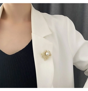 Detailed view of a gold brooch with micro-paved zircons and a central pearl on a white blazer
