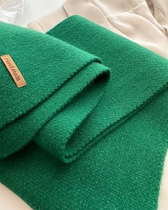 Close-up of green knitted scarf with textured fabric and a brown 'Hand Made' leather tag