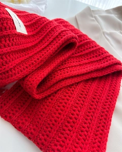 Detailed close-up of thick red chunky knit wool scarf texture with elegant white brand tag