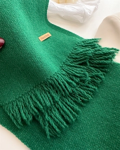 Detailed macro view of green knit scarf texture with handmade leather label and fringe