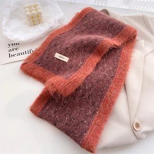 Close-up of fluffy burgundy and orange knit scarf texture with a stitched brand label