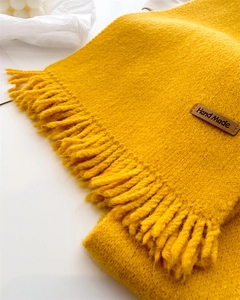 Close-up of ginger yellow knit scarf with fringe and handmade leather label detail