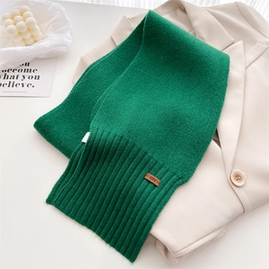 Detail eines grünen Strickschals mit Lederetikett auf einem beigen Blazer im Set