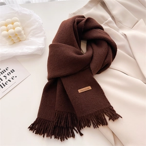 Detail of dark brown knitted scarf showing thick texture, fringe, and leather Hand Made label