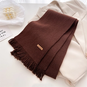 Close-up of brown knit scarf featuring handmade leather label and fringe detail