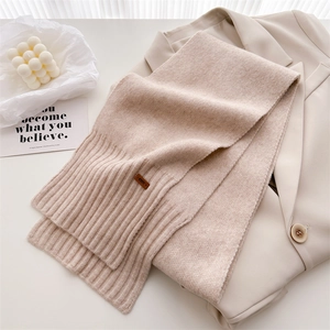 Detail eines warmen beigen Wollschals mit Rippstrick und Lederlabel auf einem Blazer