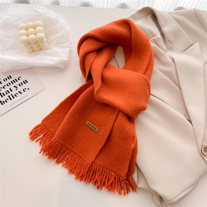 Close-up of orange knit scarf with tassel fringe and a brown leather Hand Made label
