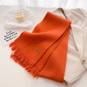 Close-up of orange knitted scarf with fringed edges and a leather Hand Made label