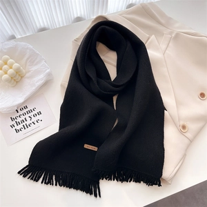 Close-up of black knitted scarf with fringe and a brown leather handmade label