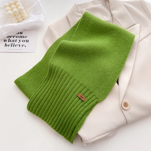 Detail eines grünen Strickschals aus Wolle mit Rippbündchen und Lederetikett