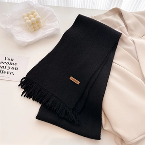 Detail of black knit scarf with soft fringe and brown handmade leather tag