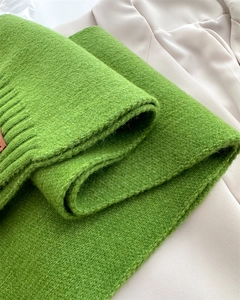 Detailaufnahme des grasgrünen Grobstrickschals mit braunem Lederetikett für Damen