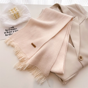 Detail of soft cream knit scarf with tassel edges and a handmade leather tag on the fabric