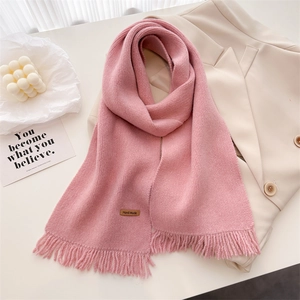 Detail view of pink knitted scarf featuring soft fringe edges and a leather handmade label