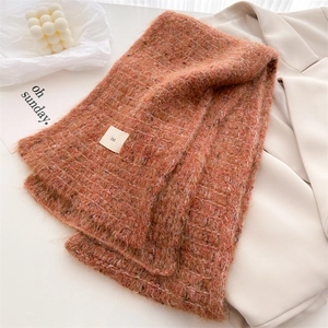 Detailed close-up of thick orange wool-blend knit scarf with minimalist fabric label