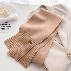 Detail eines beige gestrickten Wollschals mit braunem Lederetikett auf einem Sakko