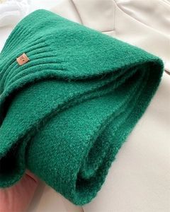 Detailansicht eines grünen Strickschals aus Wolle mit Lederetikett und Textur