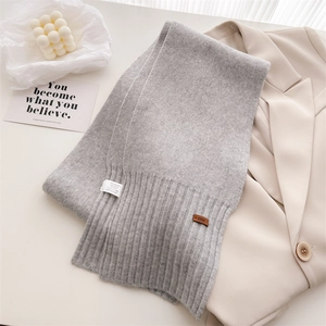 Nahaufnahme eines hellgrauen Strickschals mit braunem Lederetikett und Rippsaum