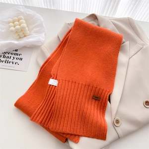 Nahaufnahme der orangefarbenen Strickschal-Struktur mit Lederetikett und Waschetikett