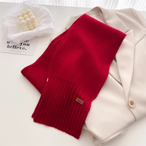Detail eines dunkelroten Strickschals aus Wolle mit Lederlogo-Patch auf beigem Blazer