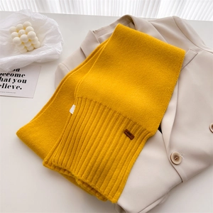 Detail eines gelben Strickschals mit Lederetikett auf einem beigen Blazer Hintergrund
