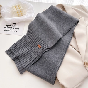 Detail eines grauen Strickschals aus Wolle mit Rippbündchen und geprägtem Lederetikett