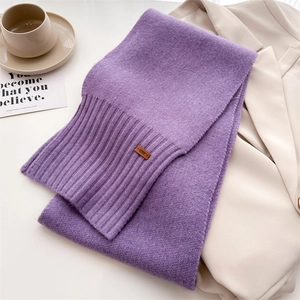 Detail eines lila Strickschals mit breitem Rippstrick und Lederetikett auf Blazer