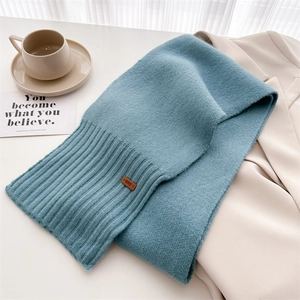 Detail eines blauen Strickschals mit gerippter Struktur und braunem Leder-Logo-Etikett