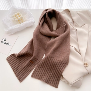 Detailansicht eines braunen Strickschals mit Rippenmuster und Vintage Leder-Label