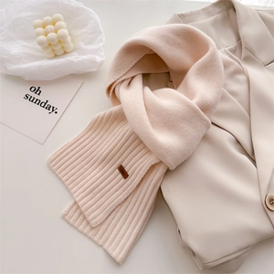 Detail eines weichen beigen Strickschals mit Rippstruktur und Leder-Markenetikett