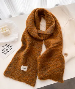 Gros plan d'une écharpe en laine orange avec étiquette tissée sur un bureau blanc