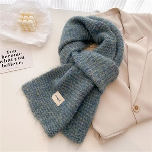 Gros plan d'une écharpe en maille bleu-vert moelleuse avec étiquette tissée minimaliste