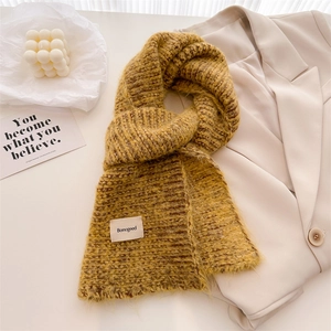 Écharpe en laine tricotée jaune moutarde avec étiquette de marque sur fond de blazer beige