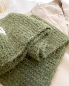 Détail d'une écharpe en maille mohair vert herbe avec étiquette blanche sur un blazer beige