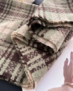 Close-up of thick plaid scarf featuring green and brown checkered knit with soft fringe