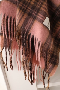 Close-up of soft plaid scarf fabric showing warm pink textures and long tassel fringe