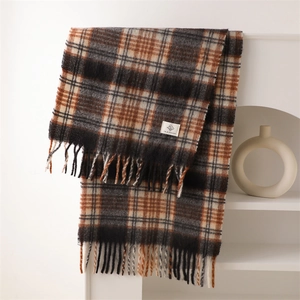 Detail of soft plaid scarf with fringe and brand label on a minimalist shelf