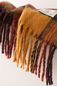 Close-up of thick plaid knit scarf with tassels and YB.BLOSSOM brand woven label