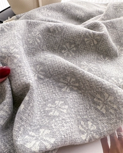 Detailed view of jacquard snowflake pattern on soft grey and cream cashmere scarf with tassels