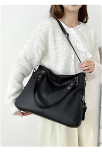 Détail d'un sac cabas en cuir noir grainé porté à l'épaule sur un pull crème